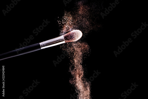 Make up brush with golden powder dust explosion isolated on black background. Beauty and fashion concept image. Close up, selective focus