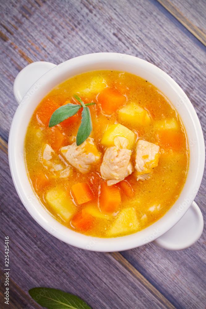 Chicken, butternut squash, apple, ginger and sage stew in white bowl on wooden table. Pumpkin soup with chicken. overhead, vertical Chicken, butternut squash, apple, ginger and sage stew in white bowl on wooden table. Pumpkin soup with chicken. overhead, vertical