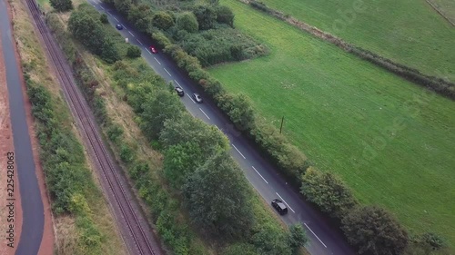 Aerial tracking along a busy english country main road, surrounded by trees, fields and a railway track. photo