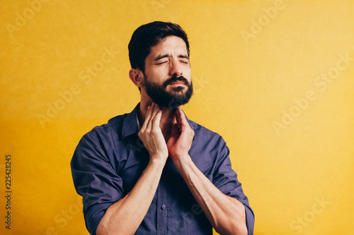 Young man having sore throat and touching his neck over yellow background. Hard to swallow photo