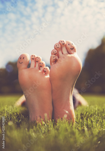 shallow DOF on a man with his smiley face painted feet crossed in a park on a hot summer day photo