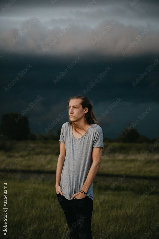 Obraz premium Attractive Young Male Model with Man Bun and Long Blonde Hair Posing for Camera Outside in Filed During Sunset