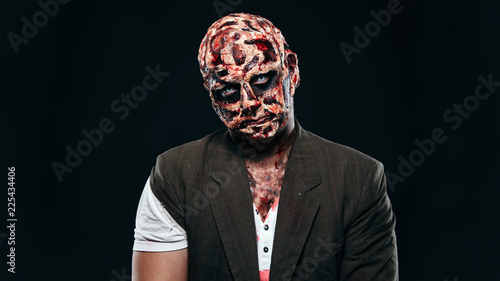 scary halloween theme and halloween makeup: scary man with a burnt face holds a baseball bat in his hands, serial maniac in a ragged suit, evil or angry superhero on a black background