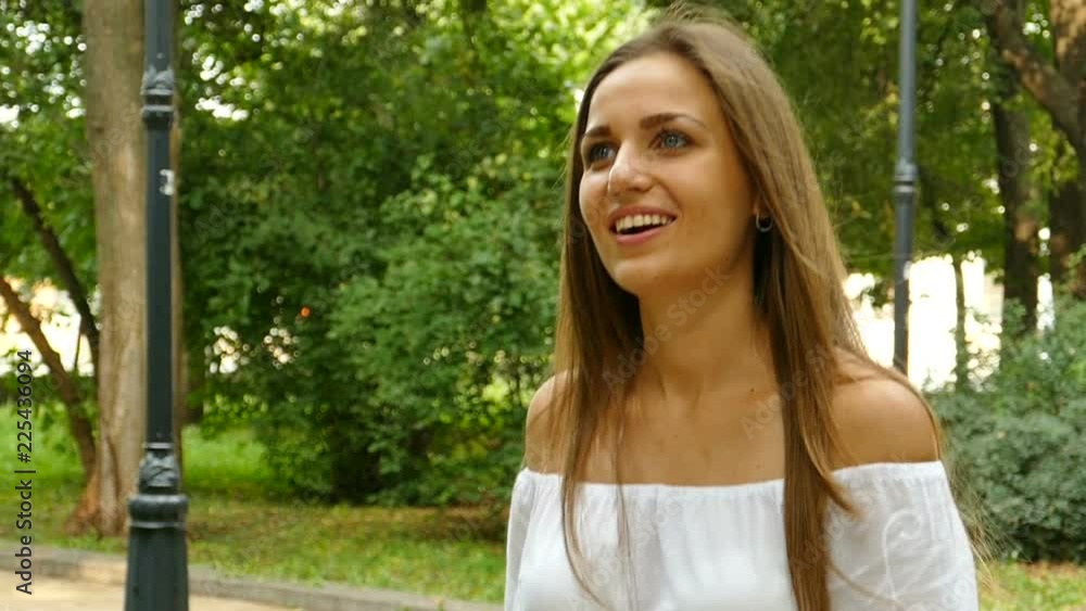 Attractive long -hair woman in city summer park walk and smiles ,looking around .Slow motion, steady shot Attractive long -hair woman in city summer park walk and smiles ,looking around .Slow motion, steady shot