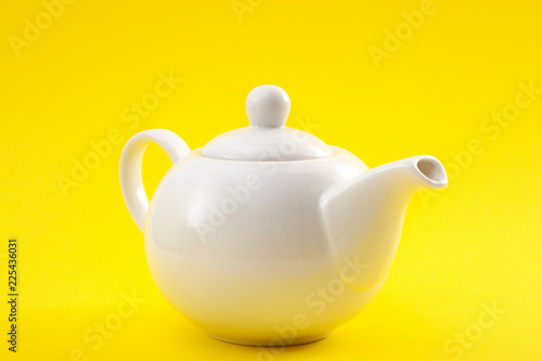 White ceramic teapot, china pot or tea kettle isolated on yellow background