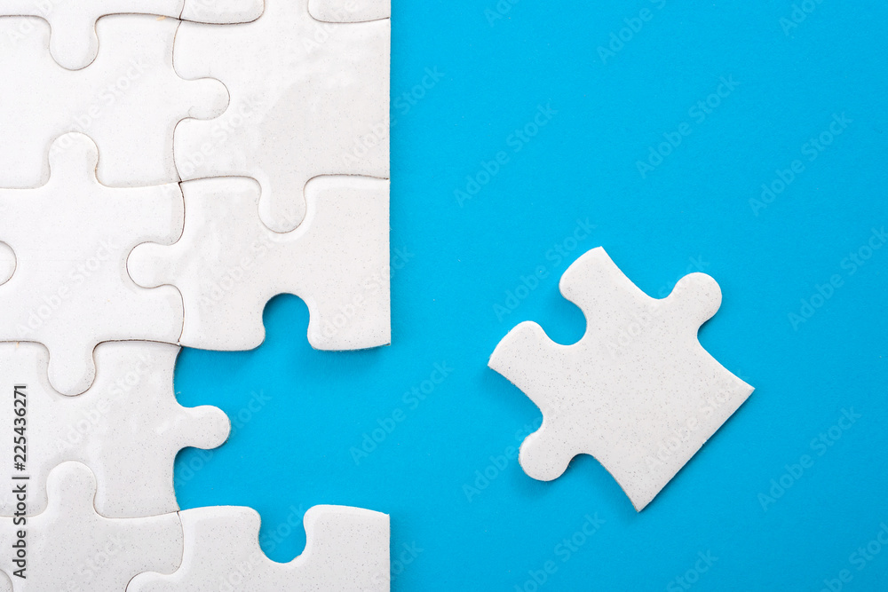 Teamwork, completing the final task and finding the solution concept with the missing piece of a jigsaw puzzle next to unfinished board isolated on blue with copy space - obrazy, fototapety, plakaty 