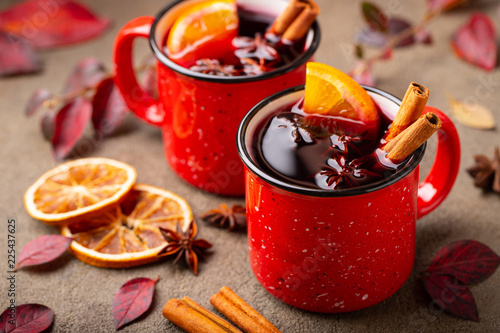 Two cups of autumn mulled wine or gluhwein with spices and orange slices on rustic table top view. Traditional drink on autumn holiday on the background of autumn leaves photo