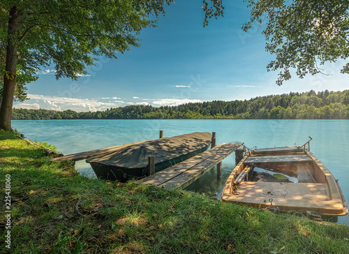 Angelegte Boote an einem herrlichen Sommertag an einem Steg in der gr  nen Natur an einem t  rkisblauen See in Bayern