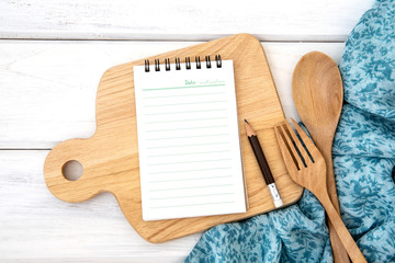 a  lined book notepad paper on chopping cutting board and tablecloth with wooden fork and spoon on white table , recipes food  for healthy habits shot note background concept