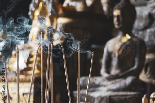 Incense sticks are burning in front of an altar with Buddha figurines, selective focus