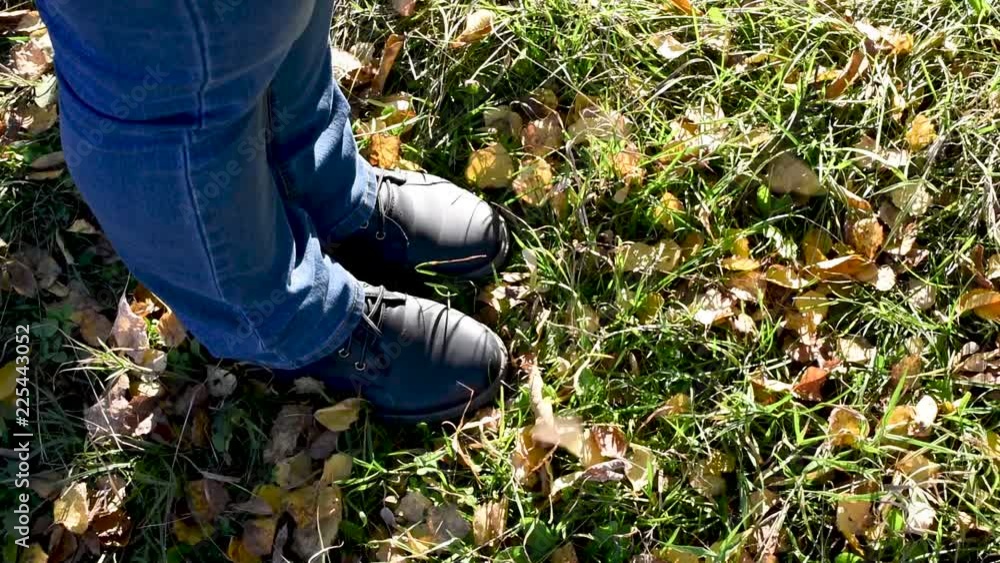 Legs in dark blue boots stand in a puddle and the grass stomp in the water, so that the spray fly in different directions, fall on his feet leaves Legs in dark blue boots stand in a puddle and the grass stomp in the water, so that the spray fly in different directions, fall on his feet leaves