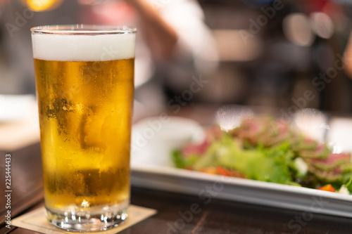 glass of cold craft beer with white bubbles and blurred food as background