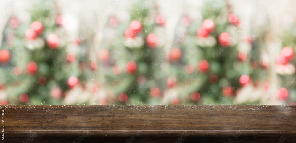 Empty rustic wood table top with abstract blur christmas tree red decor ball and snow fall background with bokeh light,winter Holiday backdrop,Mock up banner for display of product or promotion.