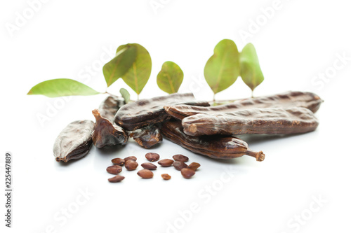 Carob bean on white. Healthy organic sweet carob pods with seeds and leaves, healthy eating and food background.