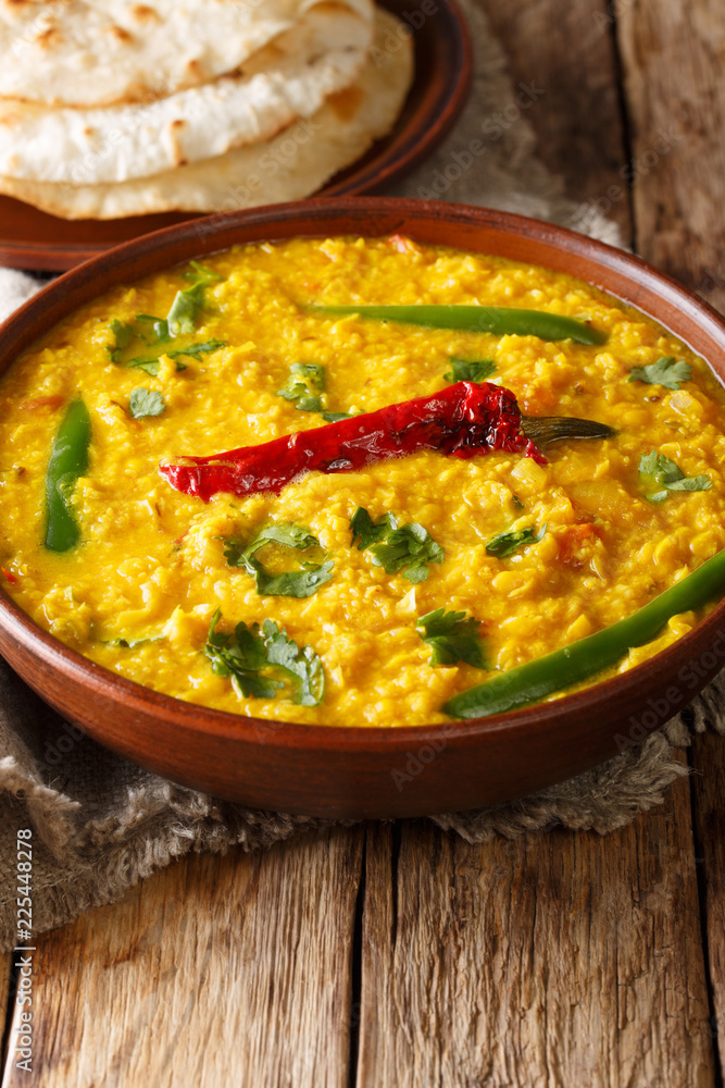 Dal Tadka yellow lentil Indian soup with flat bread on a wooden table close-up. Vertical Dal Tadka yellow lentil Indian soup with flat bread on a wooden table close-up. Vertical