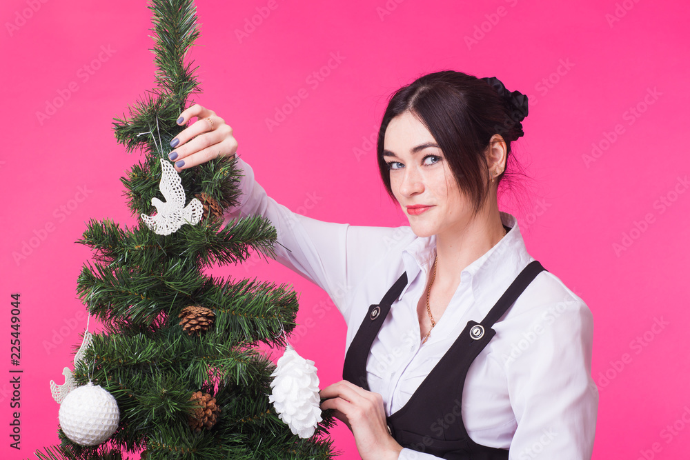 Christmas, holidays and people concept - young happy woman decorating christmas tree on pink background