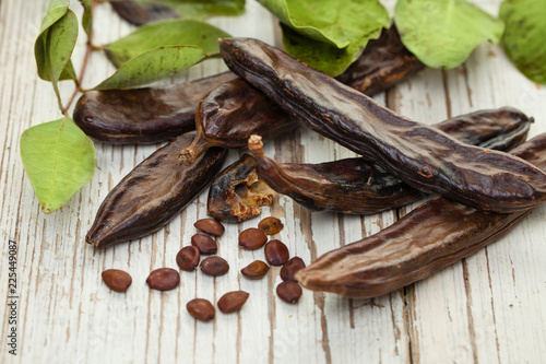 Carob pods. Healthy organic sweet carob pods with seeds and green leaves on a wooden table. Healthy eating, food background.