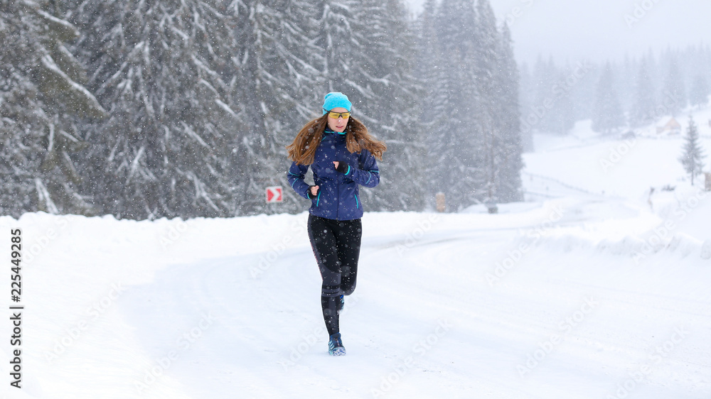 Young woman running on the mountain road in winter