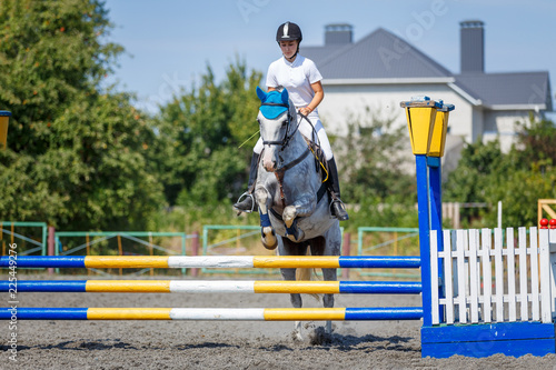 Equestrian sport. Young girl jumping over obstacle