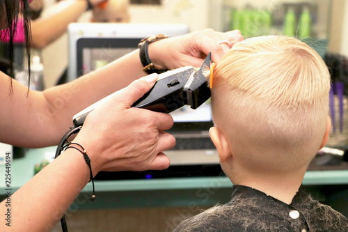 Little boy at the hairdresser, he is watching a cartoon on a laptop. Hairdresser's hands making hairstyle to little boy, close up, Fashionable haircut for boys.