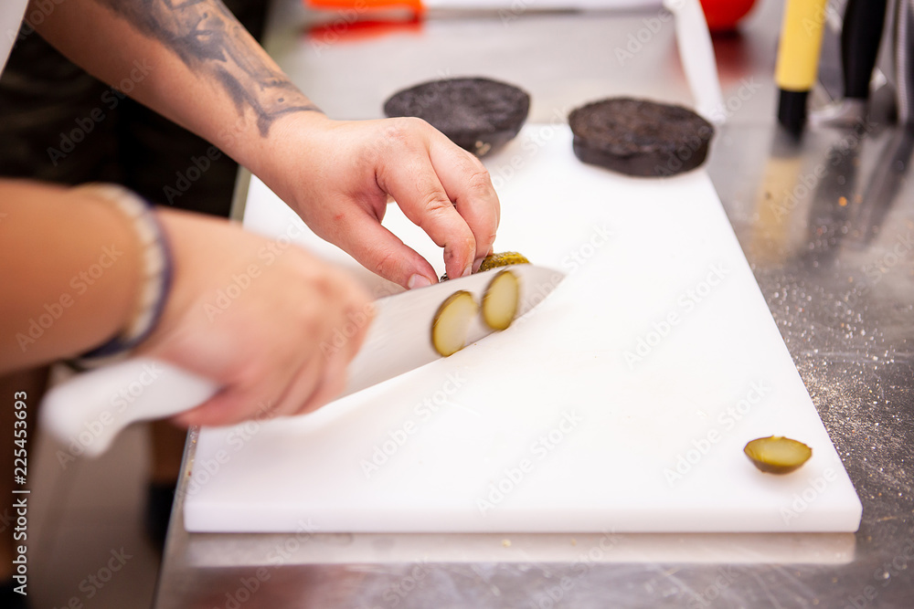 Chef slices pickles for delicious burger in restaurant. Food preparation Chef slices pickles for delicious burger in restaurant. Food preparation