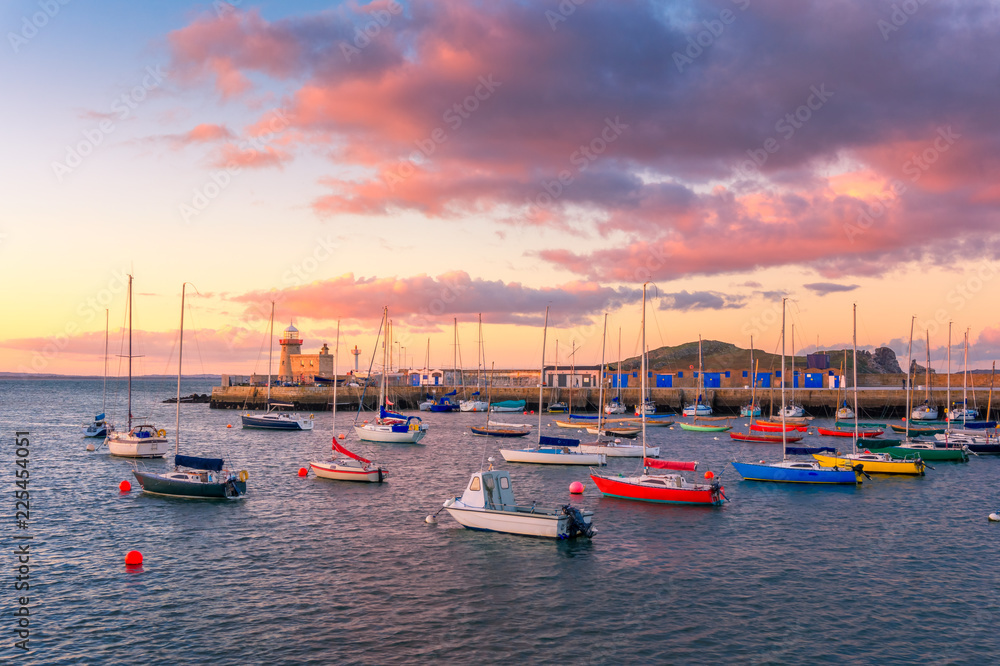 Amazing sunset in Howth, Dublin, Ireland. The view over Howth Lighthouse and colorful boats at the foreground.