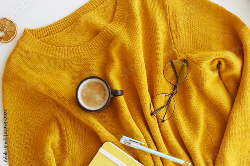 Yellow bright sweater with notepad, pen, glasses and a cup of coffee. Autumn mood and style. Top view, flat lay