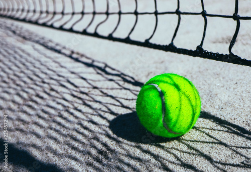 One green tennis ball on court, sport competition concept. Tennis net shadow on the ball. Macro view. © Alice Fox