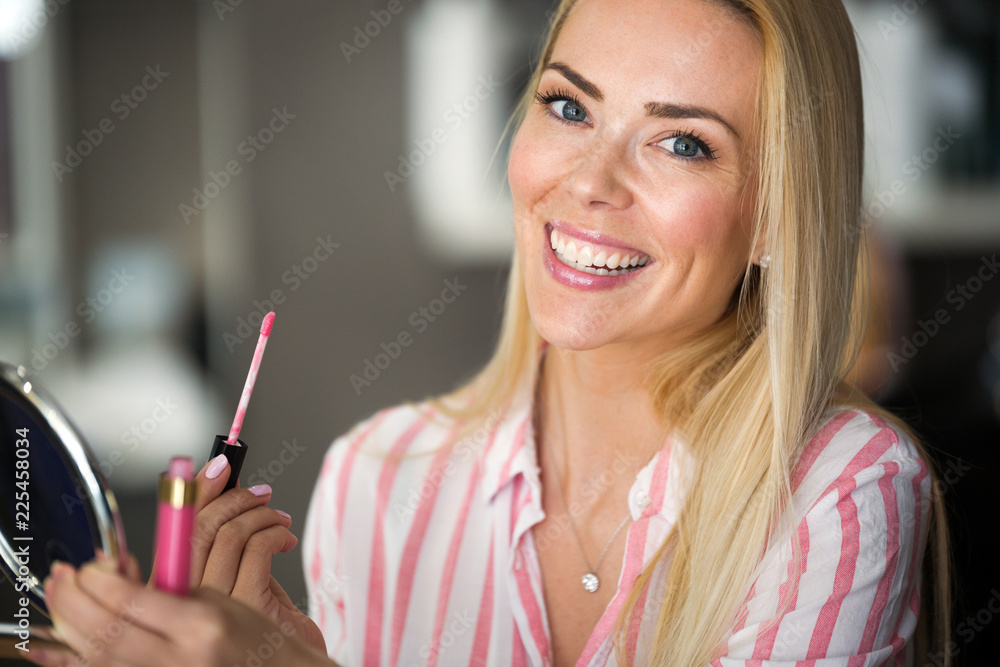 Naklejka premium beautiful young woman applying lips makeup