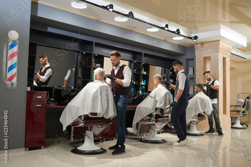 Barbers working with clients in modern barbershop.