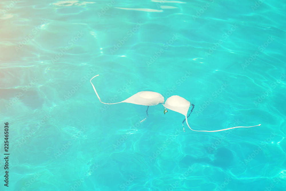 Wet female swimsuit bra or brassiere floating in water of swimming pool.  White bikini in clean