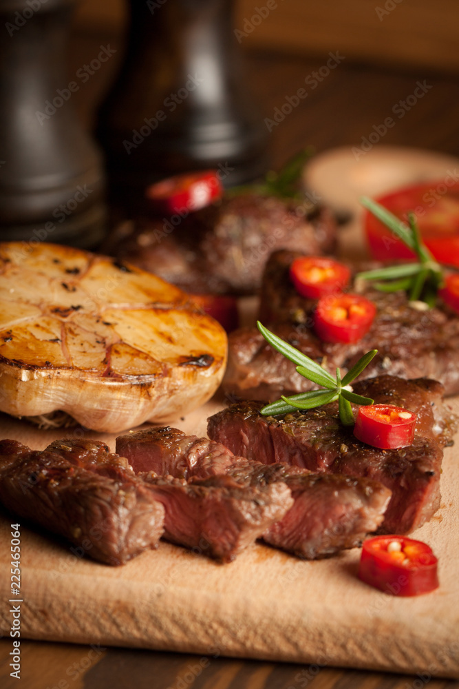grilled fillet steak with tomatoes and roast vegetables on an old wooden board, background. grilled fillet steak with tomatoes and roast vegetables on an old wooden board, background.