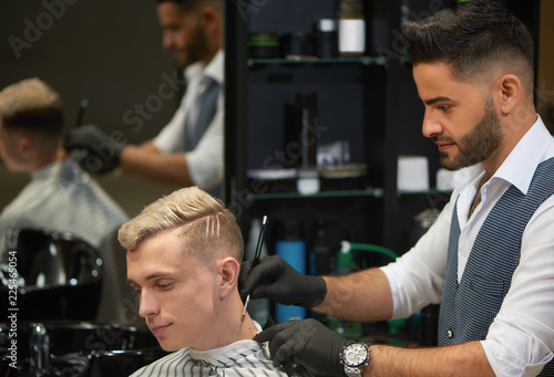 Bearded barber shaving neck of client using razor.