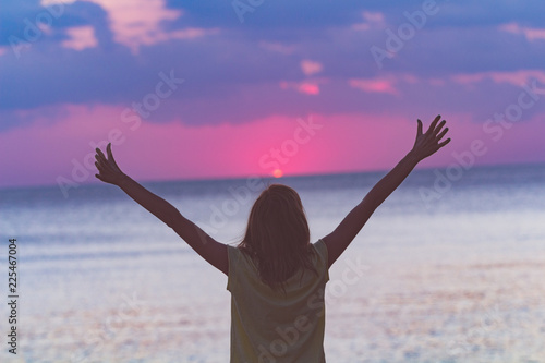 Woman with arms wide open looking at the sunset over ocean / sea.