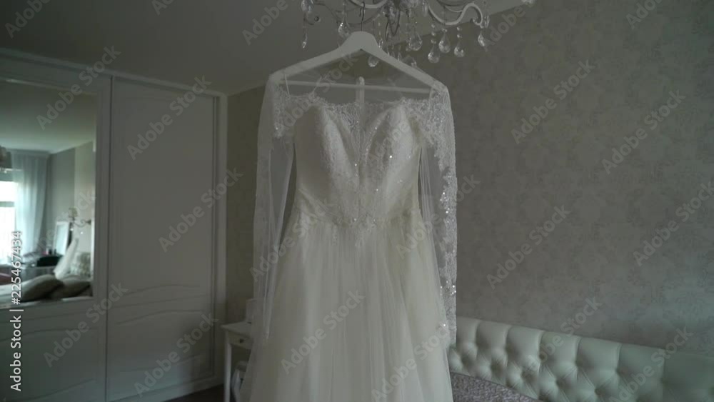 Luxury wedding dress hanging in bedroom. Silhouette of amazing bride's lace gown in light. Morning preparation, getting ready. Wedding morning Luxury wedding dress hanging in bedroom. Silhouette of amazing bride's lace gown in light. Morning preparation, getting ready. Wedding morning