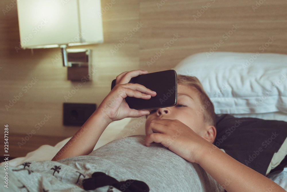 Small boy watching cartoons on smart phone while lying on the bed. Small boy watching cartoons on smart phone while lying on the bed.