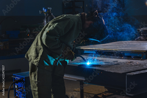 side view of welder in protection mask brazing metal at factory