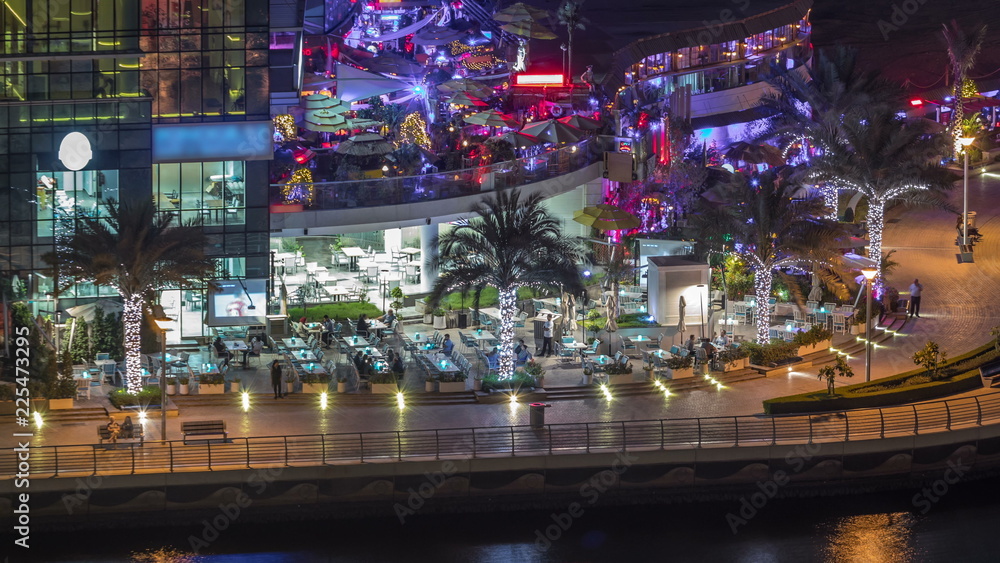 Promenade and canal in Dubai Marina with luxury skyscrapers and yachts around night timelapse, United Arab Emirates