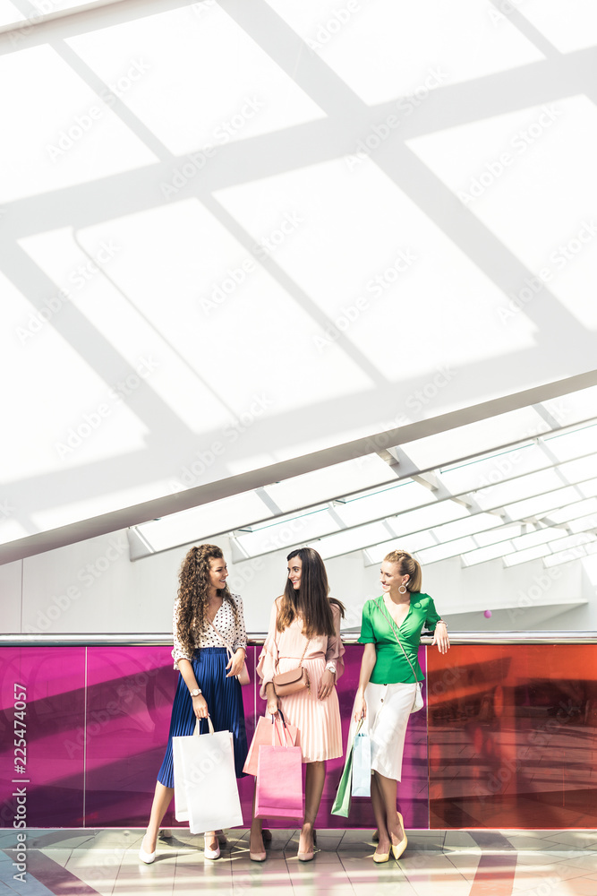 stylish young women holding paper bags and talking in shopping mall stylish young women holding paper bags and talking in shopping mall