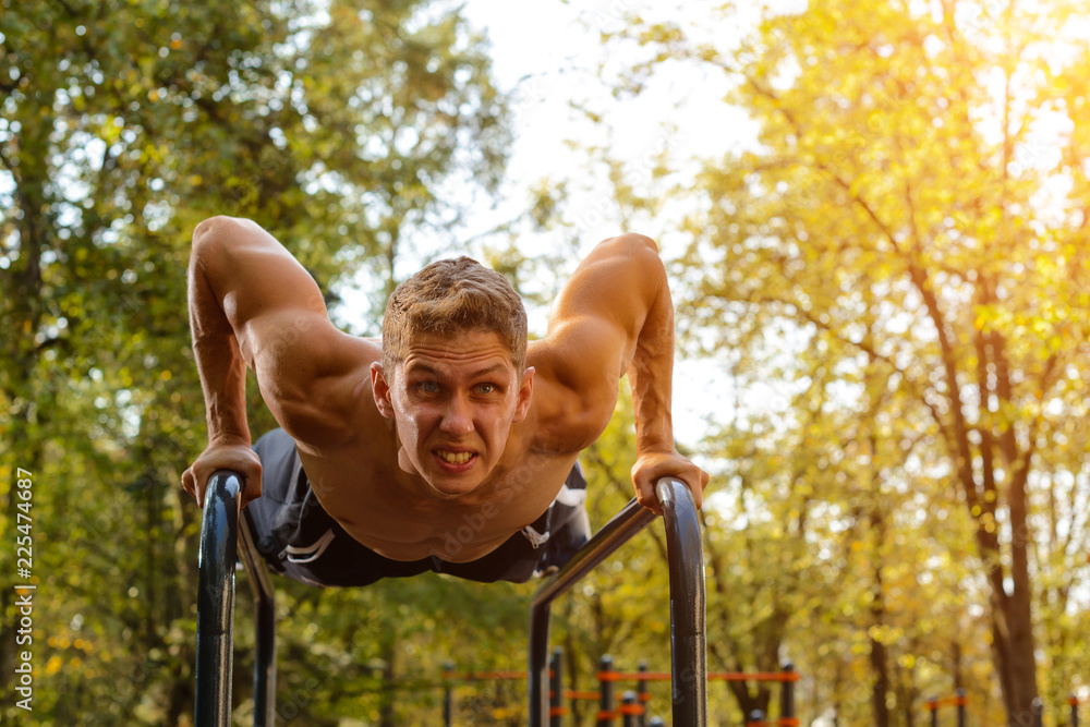 Obraz premium Athletic young Caucasian man doing push ups on parallel bars