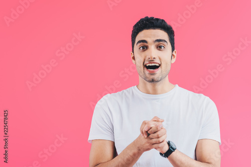 excited handsome man holding hands together and looking away isolated on pink