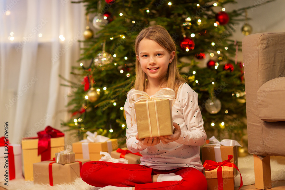 christmas, holidays and childhood concept - smiling girl with gift box at home