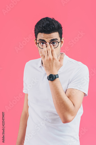 handsome man fixing glasses and looking at camera isolated on pink