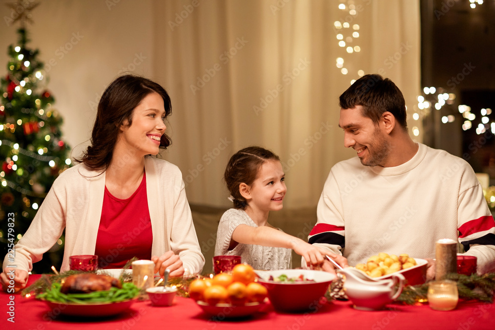holidays, family and celebration concept - happy mother, father and little daughter having christmas dinner at home holidays, family and celebration concept - happy mother, father and little daughter having christmas dinner at home