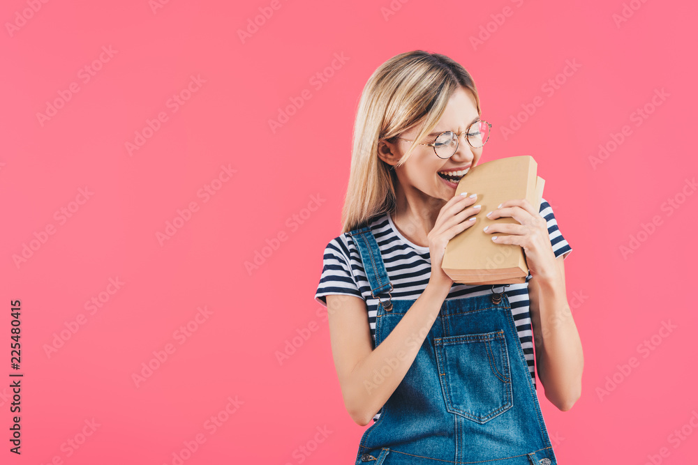 portrait of young student in eyeglasses biting books isolated on pink portrait of young student in eyeglasses biting books isolated on pink