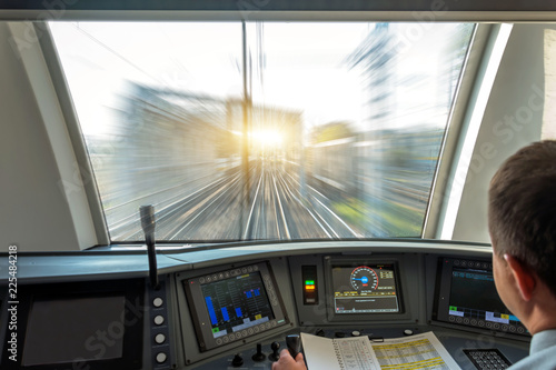 Train driver at the controls cab of speed passenger train, view of the railway bridge with the effect of speed motion blur.