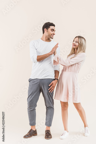 happy young couple giving high five and smiling each other isolated on beige