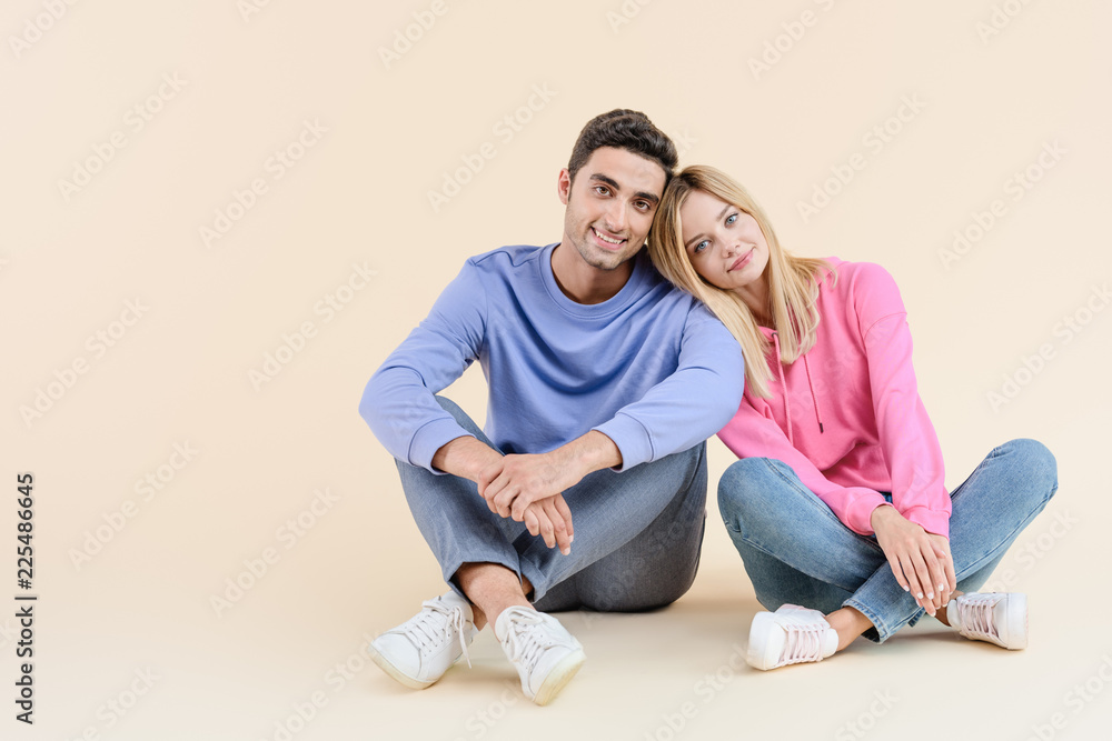 beautiful happy young couple sitting together and smiling at camera isolated on beige beautiful happy young couple sitting together and smiling at camera isolated on beige