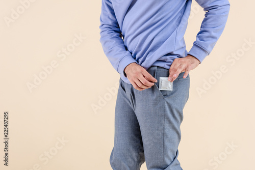cropped shot of man putting condom into pocket isolated on beige