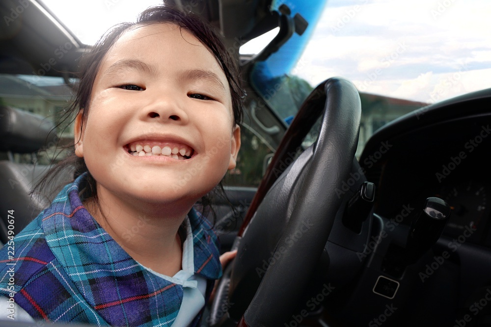 Asian little young girl smiling and sitting in the car with steering wheel.Happiness of cute kid in student uniform on sunroof car and sunlight background.Holiday,Vacation,Family,Travel Concept. Asian little young girl smiling and sitting in the car with steering wheel.Happiness of cute kid in student uniform on sunroof car and sunlight background.Holiday,Vacation,Family,Travel Concept.